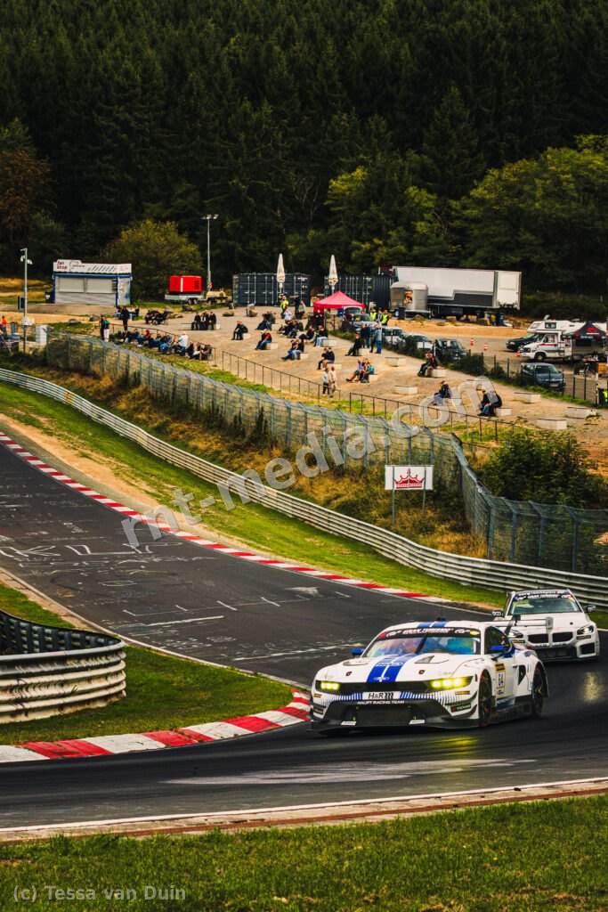 Ford Mustang GT3 #64 van Haupt Racing Team (Vincent Kolb / Frank Stippler), met een BMW erachter, toeschouwers langs de baan — NLS9 kwalificatie, Nordschleife, Nürburgring, 13 september 2026